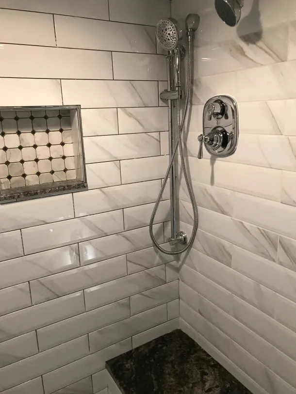 Tiled shower stall with white walls, mosaic floor, and a drain in the center.