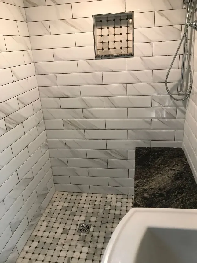 Tiled shower stall with white walls, mosaic floor, and a drain in the center.