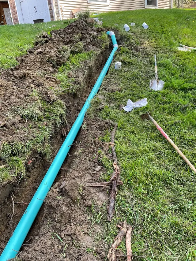 Backyard trench beside a green hose, with disturbed soil and two small sprinkler sprays.