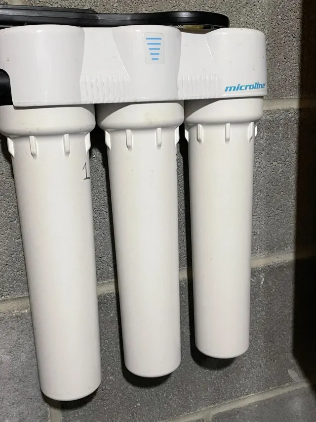 Three white water filter cartridges mounted under a sink on a countertop.